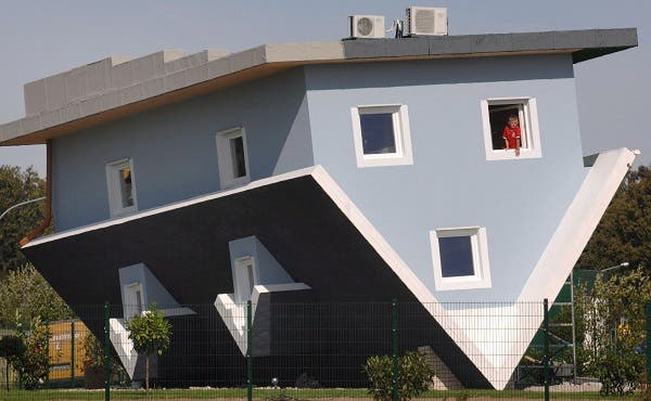 Un niño mira por la ventana de una casa colocada al revés en la isla de Usedom (Alemania), el 3 de septiembre de 2008. Empresarios polacos de Szczecin tienen prevista la apertura de la casa unifamiliar mañana. Dentro de ella todos los objetos están colocados al revés para permitir tener una visión especial de las cosas cotidianas. La casa, en la que no vive nadie, fue construida como parte del proyecto 'Un mundo al revés'. En la exposición se mostrarán peculiaridades del mundo de la arquitectura. EFE/Stefan Sauer