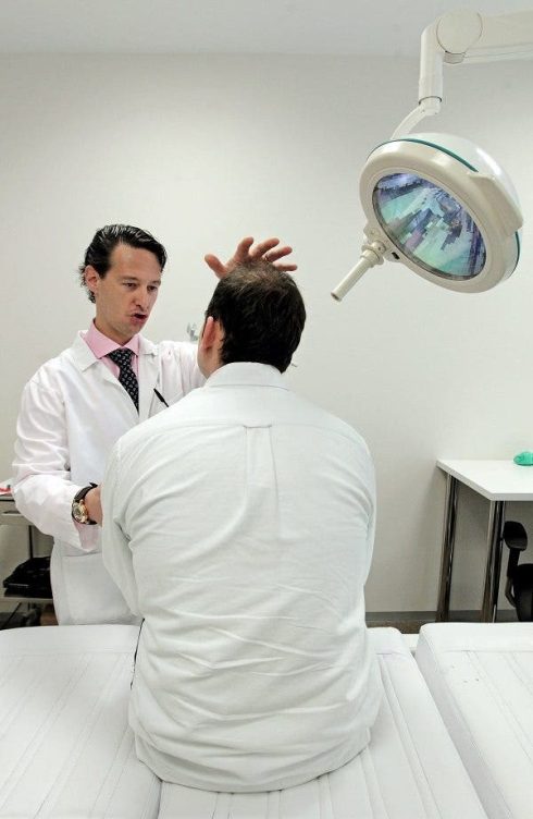 El dermatólogo José María Ricard observa la evolución del trasplante de pelo realizado a un paciente. Efesalud.com