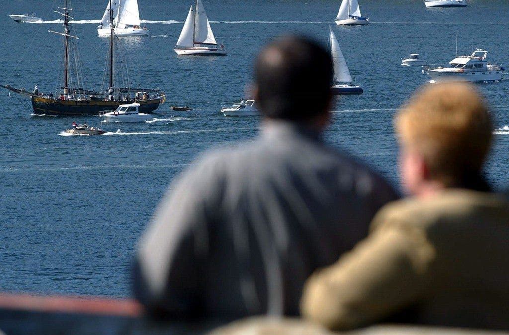 Pareja de ancianos contempla veleros en un puerto pesquero