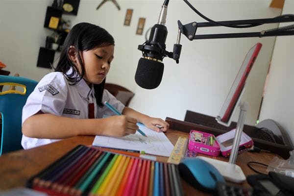 Una niña dibujando mientras tiene el móvil delante
