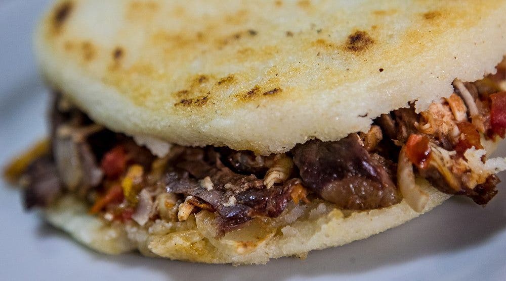 Una arepa, bocadillo o emparedado venezolano, rellena de carne y tocineta.
