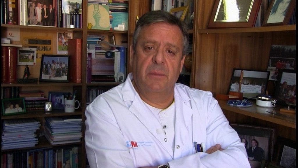 El doctor Ancochea, vestido con la bata blanca de médico del Hospital La Princesa de Madrid, retratado con los brazos cruzados sobre su pecho delante de la librería de su despacho