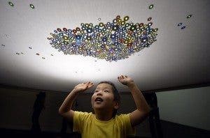 Un niño juega con unas canicas colocadas sobre una tela en la instalación de Atelier Omoya en la exposición llamada "El Museo Mágico: La Ilusión de la Luz" en el Museo Real Ueno en Tokio (Japón)