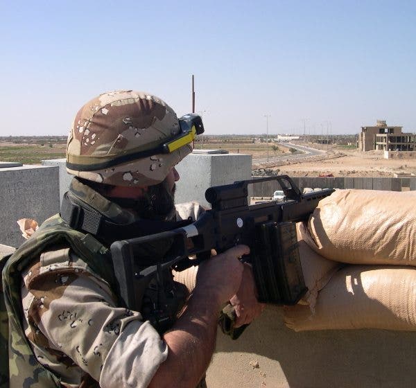 Un soldado español, con casco y uniforme de camuflaje, vigila con su fusil un acceso a una carretera desde el puesto protegido con sacos terreros.