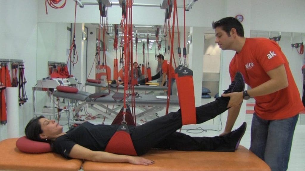 El fisioterapeuta utiliza la técnica Redcord con Isabel, que está tumbada en la camilla y su cuerpo está sujeto con una cincha por debajo de la zona lumbar y con otra por debajo de la rodilla derecha.