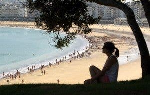 Una mujer en lo alto de una colina observa la playa soleada de La Concha, en San Sebastián. Viajar. Efesalud.com