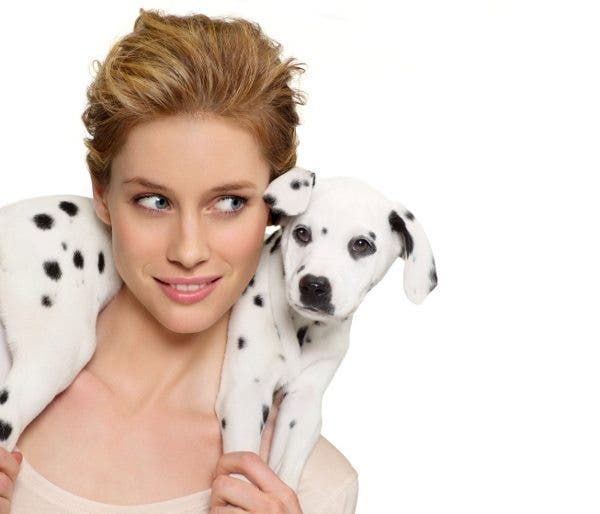 Primer plano de una mujer rubia con un cachorro de perro dálmata a los hombros, como si fuera un cordero