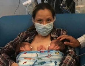 Una mujer posa con sus dos bebés gemelos recién nacidos.