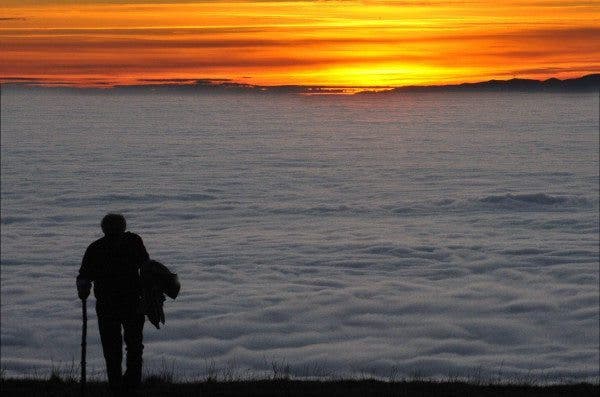 Una persona camina con un "mar de nubes" detrás y al fondo un atardecer. Efesalud.com