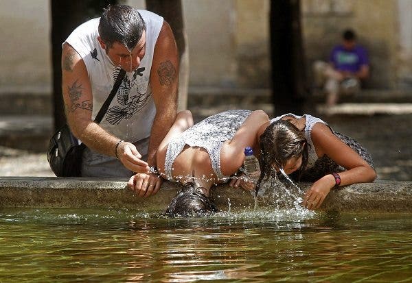 Un padre y sus dos hijos se refrescan la cabeza en una fuente