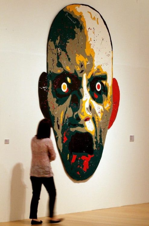 Una mujer de espaldas y de cuerpo entero contempla la obra "Cabeza collage", de José Manuel Ciria, una de las obras que forma parte de la exposición "Trozos, tramas, trazos. El collage en la Colección del IVAM". Una silueta de unos tres metros de alto de una cabeza con gesto de dolor y pánico en tonos verdes, amarillos, ocres y rojo.